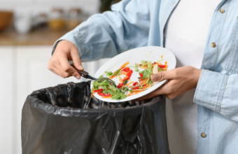 Person disposes of a plate of mixed salad into a black trash bag in a kitchen.