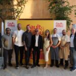 Ten people stand in a line outdoors in front of a bright yellow Gault & Millau Türkiye banner, some in chef whites and aprons, posing for a photo.