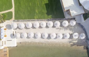 Aerial view of a sandy beach with two rows of white beach umbrellas and lounge chairs along the shore.
