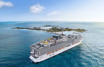 Large white MSC cruise ship sailing near a small tropical island in clear blue ocean waters.