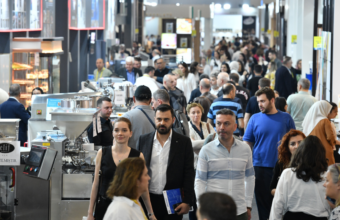 Crowded trade show floor with booths and a diverse crowd of attendees walking between displays.
